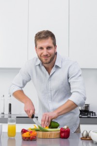 Man preparing vegetables and smiling at camera at home in the kitchen